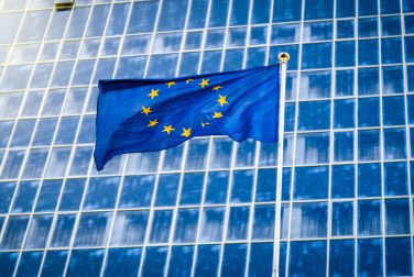 image-european-union-flag-with-staras-blue-background-against-big-modern-office-building-concept-ecenomy-development-government-politics